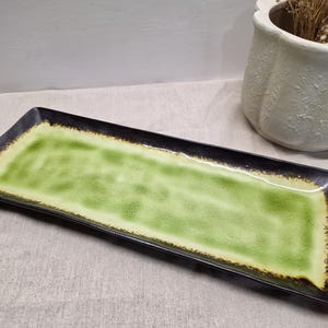Puede incluir: Una bandeja de servicio rectangular de cerámica con un centro esmaltado en verde lima vibrante que transiciona hacia un borde negro moteado y oscuro. Los bordes de la bandeja están ligeramente elevados y la superficie tiene un acabado liso y brillante.