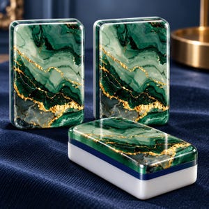 May include: Three rectangular boxes featuring a glossy green and white marble pattern with gold veining. Two boxes stand vertically, while one box lies horizontally in the foreground. Each box has a smooth, polished finish and a white base.