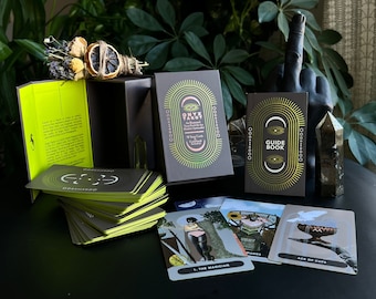 May include: A black and gold tarot deck with a guidebook. The deck features a stylized eye with a pink background and the text "Onyx Tarot: A Mystical Tarot Deck for the Modern Mystic". The guidebook has the text "Guide Book" in gold lettering.