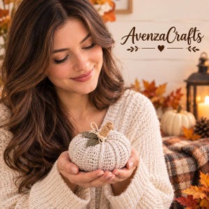 Puede incluir: Una pequeña calabaza decorativa de ganchillo en color beige con superficie texturizada, un tallo de arpillera color canela y dos hojas de tela verde oscuro atadas con un lazo de cuerda fina. El texto AvenzaCrafts aparece en la esquina superior.