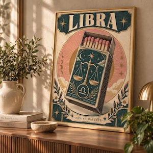 May include: A framed wall art print featuring the word LIBRA at the top and ZODIAC MATCHES at the bottom. The central illustration shows an open matchbox with pink-tipped matches, decorated with a golden scale symbol, stars, and moon motifs.