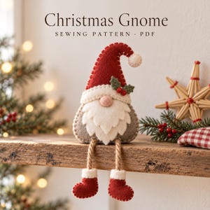 May include: A felt Christmas gnome sewing pattern PDF featuring a gnome with a red hat, white beard, and dangling legs with red boots. The gnome has a small holly leaf and berry accent on the hat. The text reads Christmas Gnome SEWING PATTERN PDF.