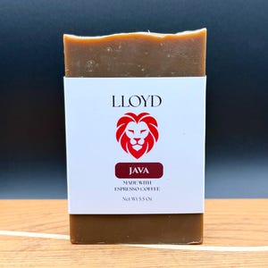May include: A rectangular bar of brown soap wrapped in a white paper label. The label features the text LLOYD above a red lion head icon, the word JAVA in a dark red box, and the text MADE WITH ESPRESSO COFFEE and Net Wt 5.5 Oz.