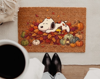 May include: A rectangular brown coir doormat featuring a printed illustration of a white beagle dog and a small yellow bird sleeping in a pile of colorful autumn leaves, surrounded by various orange, green, and blue pumpkins and a small lantern.