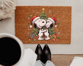 May include: A rectangular brown coir doormat featuring a colorful illustration of two white cartoon dogs wearing red Santa hats and hugging in front of a decorated Christmas tree, surrounded by small gift boxes and ornaments.