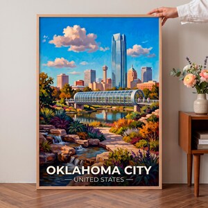 May include: A framed art print featuring a vibrant landscape painting of the Oklahoma City skyline, including the Devon Tower and a glass pedestrian bridge over a river, with lush foreground gardens and the text OKLAHOMA CITY UNITED STATES.