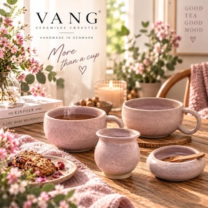 Könnte beinhalten: Zwei gesprenkelte rosa Keramiktassen, ein kleines abgerundetes Keramikgefäß und eine flache Keramikschale mit einem Holzlöffel. Die Tassen haben seitliche Griffe und das Set zeigt eine einheitliche hellrosa Oberfläche mit dunklen Sprenkeln.