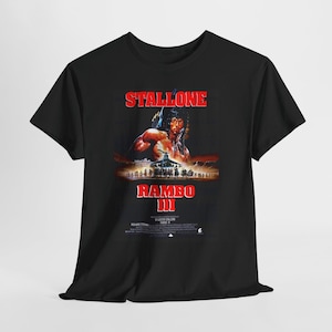 Peut inclure: Un t-shirt noir à manches courtes avec une impression graphique de l'affiche du film Rambo III. Le motif comprend le texte rouge STALLONE et RAMBO III, une illustration d'un personnage avec un arc, un hélicoptère et de petits crédits.