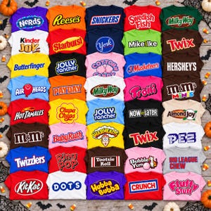 May include: A collection of thirty-five t-shirts arranged in a grid, each featuring a different colourful candy or snack brand logo, including Nerds, Reese's, Snickers, Swedish Fish, Milky Way, Kinder Joy, Starburst, York, Mike and Ike, Twix, Butterfinger, Jolly Rancher, Cotton Candy, 3 Musketeers, Hershey's, Air Heads, PayDay, Trolli, M&Ms, Hot Tamales, Chupa Chups, Now and Later, Almond Joy, Baby Ruth, Warheads, PEZ, Twizzlers, Ring Pop, Tootsie Roll, Bubble Yum, Big League Chew, Kit Kat, Dots, Hubba Bubba, Crunch, and Fluffy Stuff.