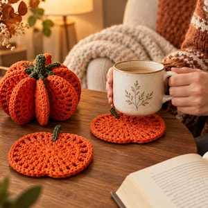 Può includere: Un set di tre articoli realizzati a mano all'uncinetto che include una zucca arancione tridimensionale con un gambo verde e due sottobicchieri piatti e circolari a forma di zucca arancione, ciascuno con un piccolo dettaglio a gambo verde.