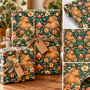 May include: Wrapping paper featuring a repeating pattern of brown capybaras adorned with flower crowns, surrounded by pink and yellow blossoms and green foliage on a dark teal background, shown on gift boxes and a paper roll with gift tags.