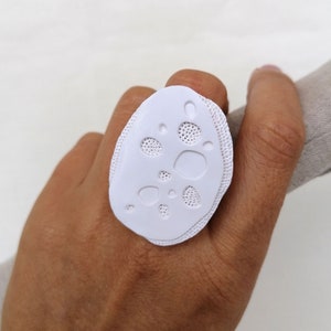 Peut inclure: Bague blanche de forme organique texturée avec un motif de petits cercles et ovales.