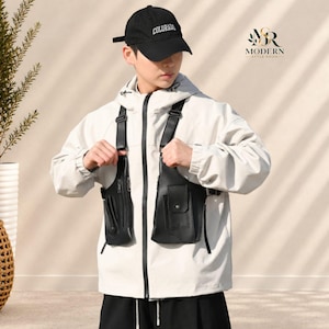 May include: A black baseball cap with the word COLORADO in white text, worn with a white hooded jacket featuring a black front zipper and a black dual-pouch chest harness with adjustable straps, metal buckles, and multiple pockets.