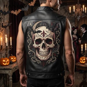 May include: A black leather vest featuring a large, detailed graphic on the back. The design displays a central skull with ornate scrollwork, surrounded by bats, a crescent moon, and small stars. The vest has a structured collar and button tabs.