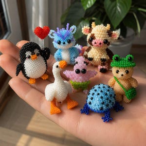 May include: A collection of seven small, handcrafted beaded figurines including a black and white penguin holding a red heart, a blue dragon, a cream-coloured cow, a white goose, a pink starfish, a blue spotted frog, and a tan bear wearing a green hat.