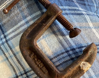 May include: A rusty metal C-clamp with a threaded screw and a handle. The clamp is marked with the text "1 3/4" on the side.
