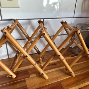 May include: A natural bamboo wine rack with a diamond-shaped design. The rack is expandable and can hold multiple bottles. The bamboo has a warm, light brown color, and the rack is constructed with small screws.