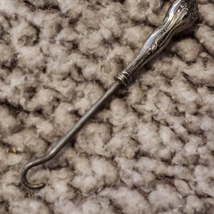 May include: A silver shoe horn with an ornate handle. The handle is shaped like a flower and has a detailed design.