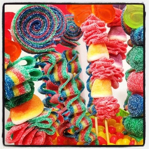 Pu&ograve; includere: Primo piano di una variet&agrave; di caramelle colorate su bastoncini. Le caramelle sono disposte in un'esposizione decorativa, con alcuni pezzi attorcigliati a spirale e altri a forma di fiori. Le caramelle sono ricoperte di cristalli di zucchero e hanno una variet&agrave; di colori, tra cui rosso, blu, verde, giallo e arancione.