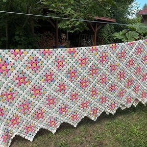 Puede incluir: Una gran colcha hecha a mano construida con numerosos pequeños yo-yos de tela circulares cosidos juntos. La colcha presenta un patrón repetitivo de círculos de tela blancos, rosas, amarillos y azul claro con motivos florales y un borde festoneado.