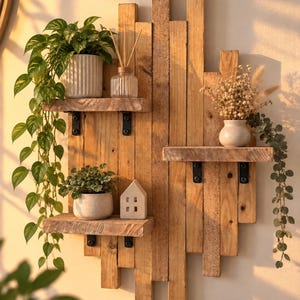 Peut inclure: Une étagère murale composée de planches de bois verticales disposées en quinconce avec trois tablettes horizontales fixées par des supports en métal noir. Les tablettes accueillent des plantes vertes, un diffuseur en verre et une figurine de maison.