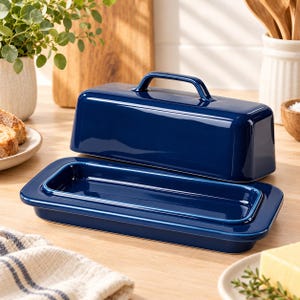May include: A glossy, deep navy blue ceramic butter dish consisting of a rectangular base with a raised rim and a matching lid featuring a central handle. The smooth, solid-colored kitchen accessory has a clean, modern design with rounded edges.