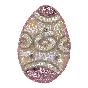May include: An egg-shaped patch featuring intricate beadwork and iridescent sequins in shades of light pink, cream, and white. The design includes swirling patterns and a border of small pink beads, creating a textured, reflective surface.