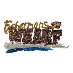 May include: A decorative patch featuring the text Fishermans Wharf embroidered with gold, brown, and iridescent sequins. The word Fishermans is in gold script, while WHARF is in brown block letters, accented by a small crab and blue waves.