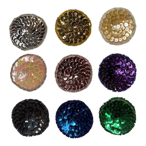 May include: A collection of nine circular patches arranged in a grid, each covered in shimmering sequins. The colors include silver, gold, iridescent white, pale pink, bronze, purple, black, royal blue, and emerald green, all with beaded edges.