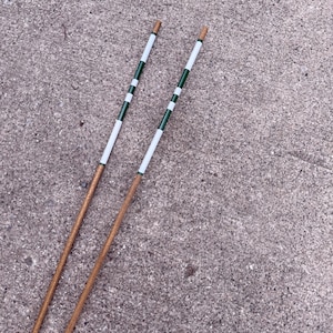 May include: A pair of long, slender wooden sticks with a natural brown finish on the lower sections. The upper portions feature a decorative pattern of alternating white and dark green bands, ending in a solid brown tip at the very top end.