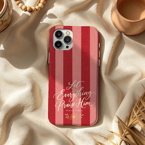 May include: A smartphone case featuring vertical stripes in alternating shades of red and light pink. The text Let Everything Praise Him Psalm 150:6 is printed in white cursive script, accompanied by a small gold sun icon at the bottom center.