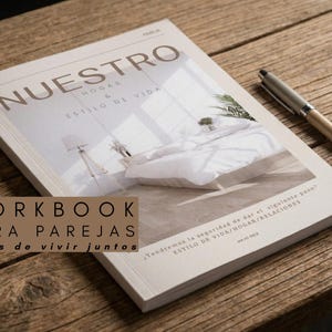 Pode incluir: Um caderno de exercícios intitulado NUESTRO HOGAR & ESTILO DE VIDA com o subtítulo WORKBOOK PARA PAREJAS antes de vivir juntos. A capa apresenta uma fotografia de um quarto com uma cama branca e um candeeiro, acompanhada por uma caneta prateada e bege.