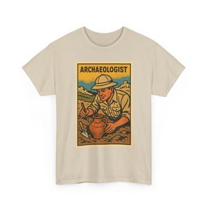 Peut inclure: Un t-shirt beige à manches courtes avec une impression graphique rectangulaire représentant un archéologue portant un casque colonial, creusant la terre avec une petite truelle à côté d'un pot en terre cuite. Le texte ARCHAEOLOGIST est en noir.