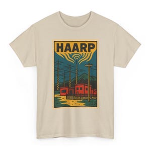 May include: A beige short-sleeve t-shirt featuring a rectangular graphic print. The design depicts a red building complex with radio towers and antennas under a dark blue sky with yellow waves. The text HAARP is printed in bold black letters.