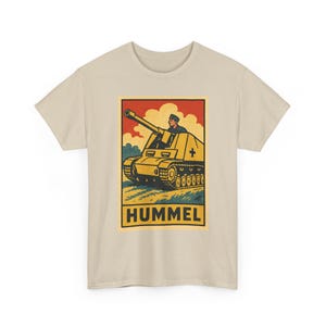 Könnte beinhalten: Ein beiges T-Shirt mit kurzen Ärmeln und einem rechteckigen Grafikdruck. Die Illustration zeigt ein gelbes Selbstfahrgeschütz mit einem Soldaten in der Luke vor einem roten Himmel und Wolken. Das Wort HUMMEL ist in Schwarz aufgedruckt.