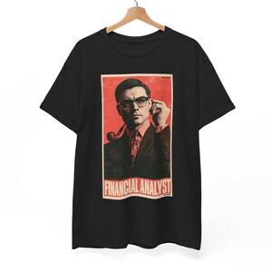 May include: A black short-sleeve t-shirt featuring a rectangular graphic print of a person in a suit, glasses, and tie, smoking a pipe. The background of the print is red with a distressed texture. The text FINANCIAL ANALYST is printed in white.