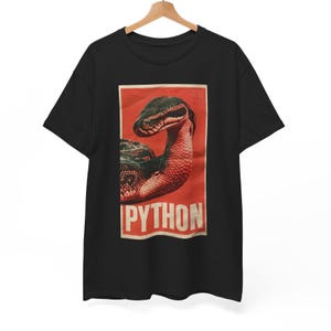 May include: A black short-sleeve t-shirt featuring a rectangular graphic print on the chest. The print displays a dark-scaled python snake against a red background with the word PYTHON printed in large, bold, off-white capital letters below.