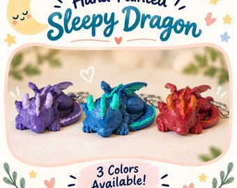 May include: Three hand-painted sleepy dragon keychains in purple, blue with teal accents, and red with orange accents. The text reads Hand-Painted Sleepy Dragon and 3 Colors Available. Each dragon figure is in a curled, resting position.