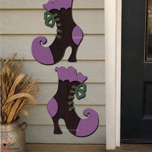 May include: Two wooden wall decorations shaped like curled-toe boots. Each boot features a dark brown body, purple accents on the cuff and toe, and a green lace-up detail. The design includes laser-cut lines and a flat, layered appearance.