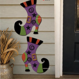 May include: Two decorative witch boot cutouts featuring purple bodies with black stars and swirls, orange and black striped cuffs, green heels and toes, and tan buckles. The text Cut and Score appears with black and red squares.
