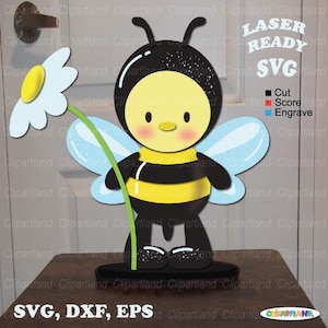 May include: A laser-ready SVG file of a cartoon bee holding a daisy. The bee has a yellow face and body with black stripes, blue wings, and black antennae. The daisy has white petals and a yellow center. The file is labeled "SVG, DXF, EPS."