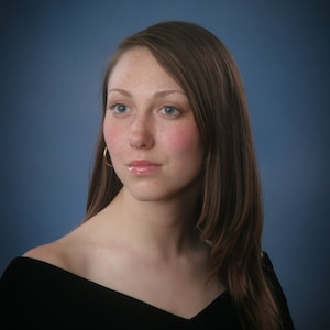 May include: A portrait of a person with long brown hair, blue eyes, and freckles. They are wearing a black off-the-shoulder top and gold hoop earrings. The background is a gradient of blue.