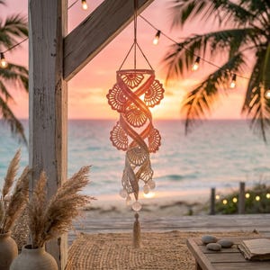 May include: A hanging spiral mobile featuring crocheted shell-shaped motifs in a gradient of peach to cream colors. The structure is suspended by thin cords and terminates in a single tassel at the bottom, with small spherical beads integrated throughout.