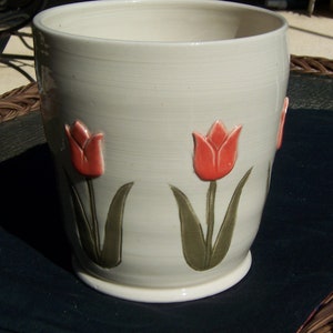 May include: White ceramic planter with a light gray glaze and four raised tulip designs. The tulips are red with green leaves.
