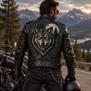 May include: A black leather jacket featuring a large, detailed graphic on the back of a wolf's head surrounded by pine trees and a full moon. The jacket has long sleeves with zippered cuffs, a collar, and a structured fit with visible seams.
