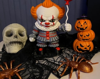 May include: A clown soap dispenser with orange hair, a white face, and a grey costume, holding a red balloon. The set includes a white skull, a stack of three orange jack-o'-lanterns, and two glittery copper spiders on black lace fabric.