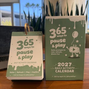 May include: A sage green 2027 daily activity calendar with a matching box. The calendar features the text 365 ways to pause & play, Relax | Refresh | Play | Explore, and 2027 by Chaoqun Yin | @Pause&Play. The box shows 365 ways to pause & play.