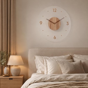 Könnte beinhalten: Eine kreisförmige Wanduhr mit einem durchscheinenden Zifferblatt und goldenen Ziffern an den Positionen 12, 3, 6 und 9. Die Mitte der Uhr besteht aus einer runden hellen Holzplatte mit zwei dünnen, dunklen Zeigern für die Uhrzeit.