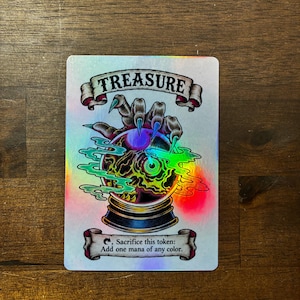 May include: A rectangular holographic game card featuring a clawed hand reaching for a crystal ball containing a green eye. The top banner reads TREASURE and the bottom banner reads Tap symbol, Sacrifice this token: Add one mana of any color.