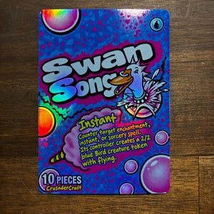 May include: A rectangular holographic trading card featuring the text Swan Song and Instant. The card displays a cartoon swan, pink bubbles, and blue confetti patterns. Text reads: Counter target enchantment, instant, or sorcery spell. Its controller creates a 2/2 blue Bird creature token with flying. 10 PIECES CrusaderCraft.